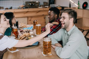 çok kültürlü arkadaşlar ile birlikte pub octoberfest kutlarken kızarmış soğan halka ile gülümseyen adam besleme genç kadın