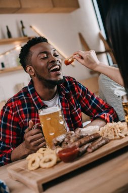 pub octoberfest kutlarken kızarmış soğan halkası ile afrikalı amerikalı adam besleme genç kadın kırpılmış görünümü