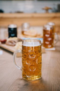 selective focus of mug with lager beer on wooden table in pub clipart