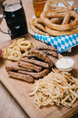 fried sausages, onion rings, french fries, pretzels and mugs with beer on wooden table in pub clipart