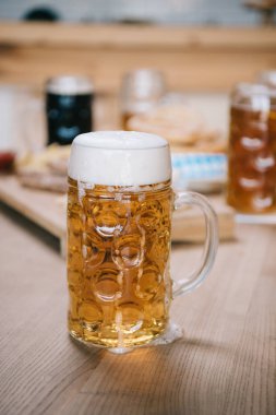 selective focus of mug with lager beer on wooden table in pub clipart