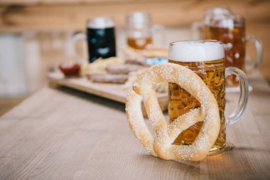 selective focus of mug with lager beer and pretzel on wooden table near tray with snacks in pub clipart