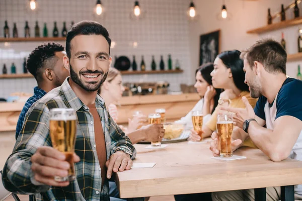 选择性的焦点英俊的男人微笑着在镜头前 而拿着啤酒杯 — 图库照片
