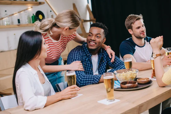 Joven Mujer Abrazando Africano Americano Hombre Cerca Multicultural Amigos Pub — Foto de Stock