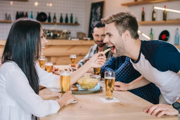 Young Woman Feeding Cheerful Man French Fries While Sitting Pub — Stock Photo, Image