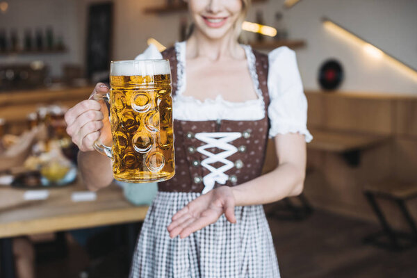 cropped view of  waitress in german national costume holding mug of light beer 