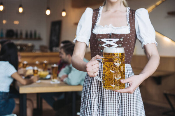 patial view of  waitress in german national costume holding mug of light beer 