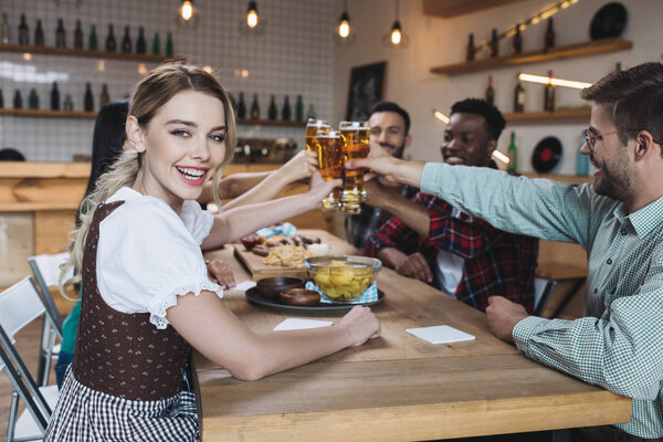 happy multicultural friends clinking glasses of light beer while celebrating octoberfest in pub