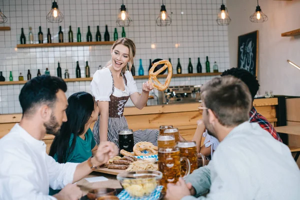 Cheerful Waitress Traditional German Costume Holding Pretzel While Standing Friends — Stock Photo, Image