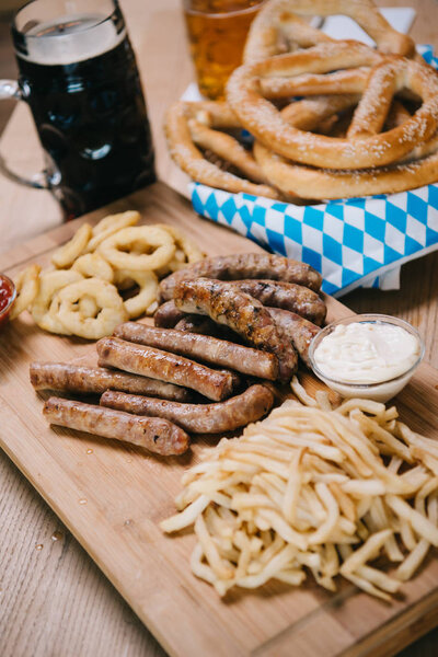 fried sausages, onion rings, french fries, pretzels and mugs with beer on wooden table in pub