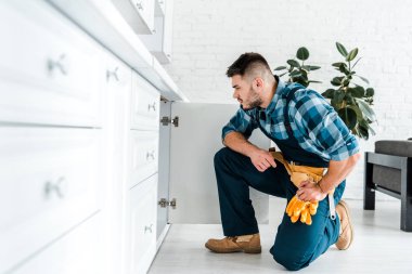 mutfak dolabı yakınında oturan alet kemeri ile yakışıklı handyman seçici odak
