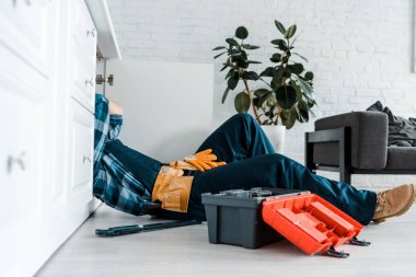 cropped view of handyman working in kitchen near toolbox while lying on floor  clipart