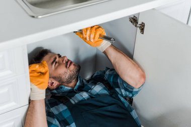 mutfakta çalışırken ayarlanabilir anahtarı tutan sakallı tamirci 