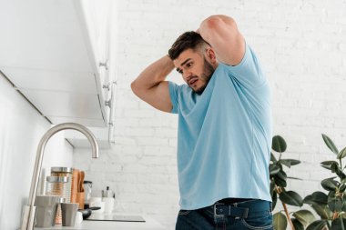 stressed man touching head while looking at sink in modern kitchen  clipart