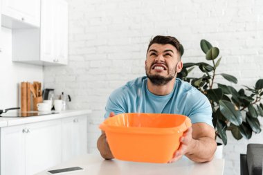 selective focus of upset man looking at water pouring into plastic wash bowl  clipart