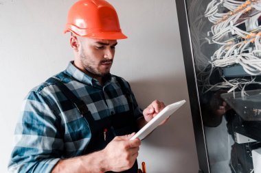 handsome workman using digital tablet near cables and wires  clipart