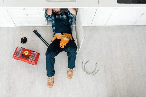 top view of handyman lying on floor near toolbox 