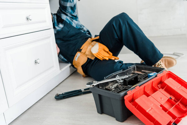 selective focus of repairman working near kitchen cabinet and toolbox