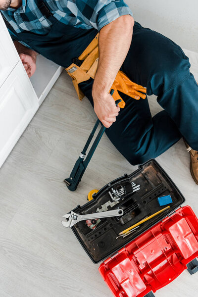 cropped view of repairman working near kitchen cabinet and toolbox with instruments 