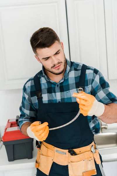 handsome repairman in rubber gloves looking at metal hose