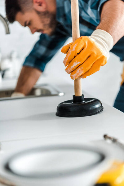 selective focus of man holding plunger in kitchen 