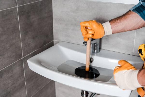 cropped view of man holding plunger in sink with water 