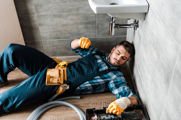 bearded handyman lying on floor near toolbox in bathroom 