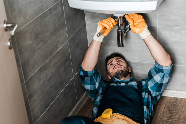 selective focus of repairman fixing water damage with wrench in bathroom 
