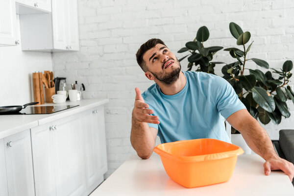 displeased man gesturing near plastic wash bowl on table 