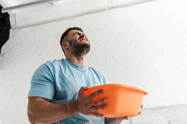 bearded man with closed eyes holding plastic wash bowl near pouring water 