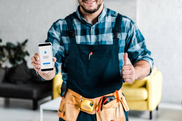 KYIV, UKRAINE - JULY 31, 2019: cropped view of happy man holding smartphone with messenger app on screen and showing thumb up 