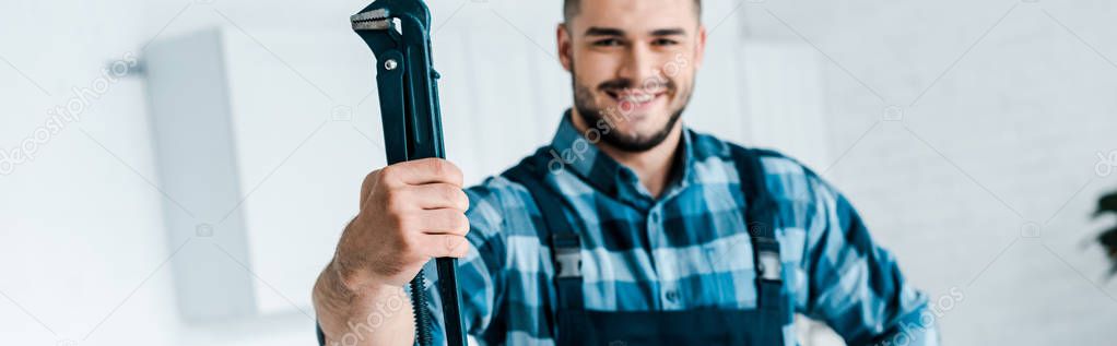 panoramic shot of happy handyman in uniform holding wire cutters 