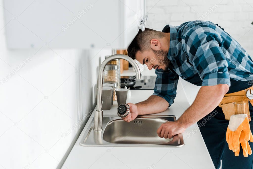 selective focus of handsome bearded repairman working near sink in kitchen 