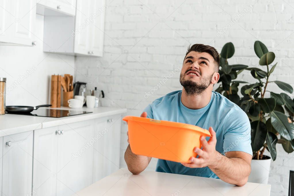 displeased man holding plastic wash bowl in kitchen 