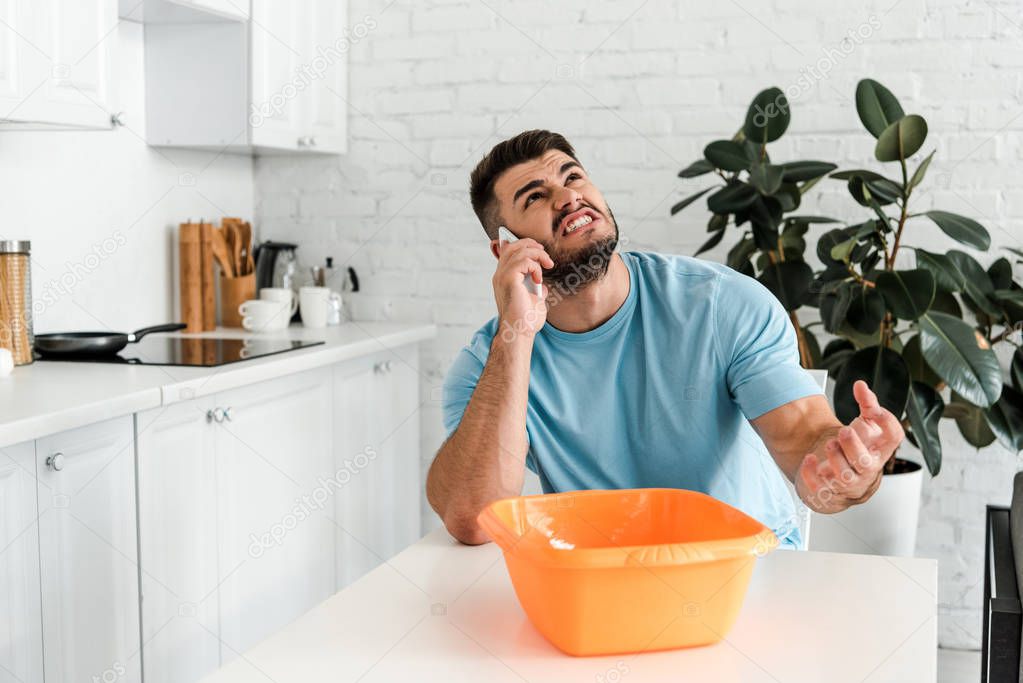 angry bearded man talking on smartphone near plastic wash bowl 