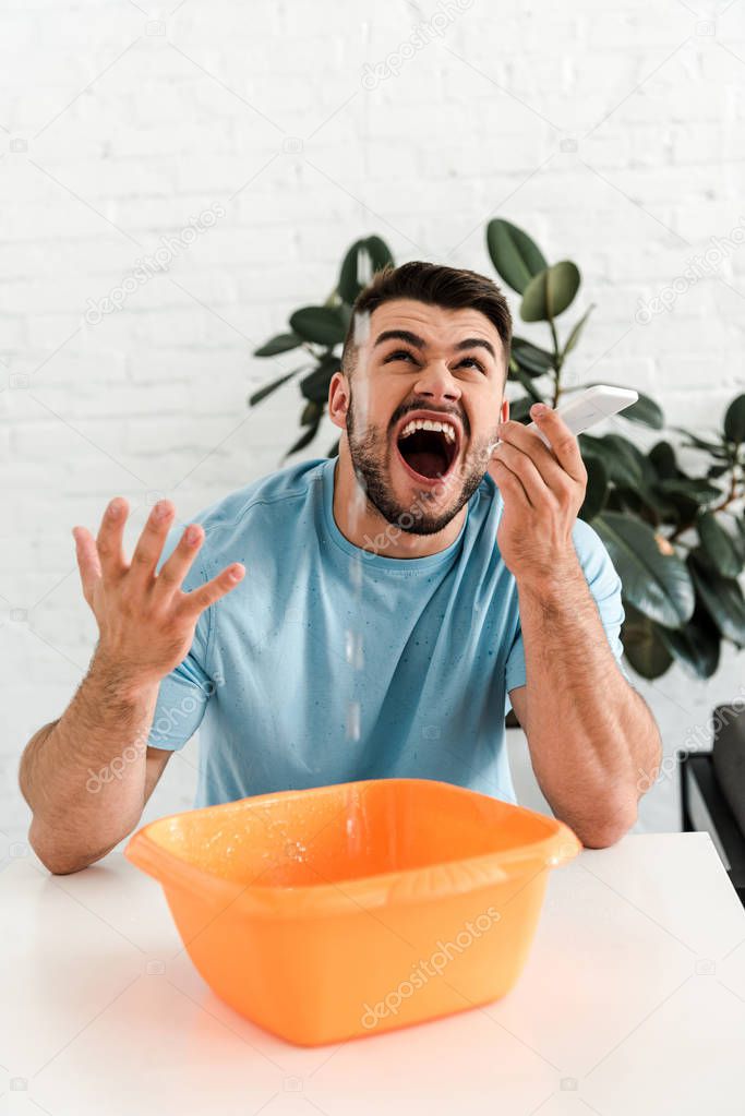 selective focus of upset bearded man screaming while looking at water pouring into plastic wash bowl 