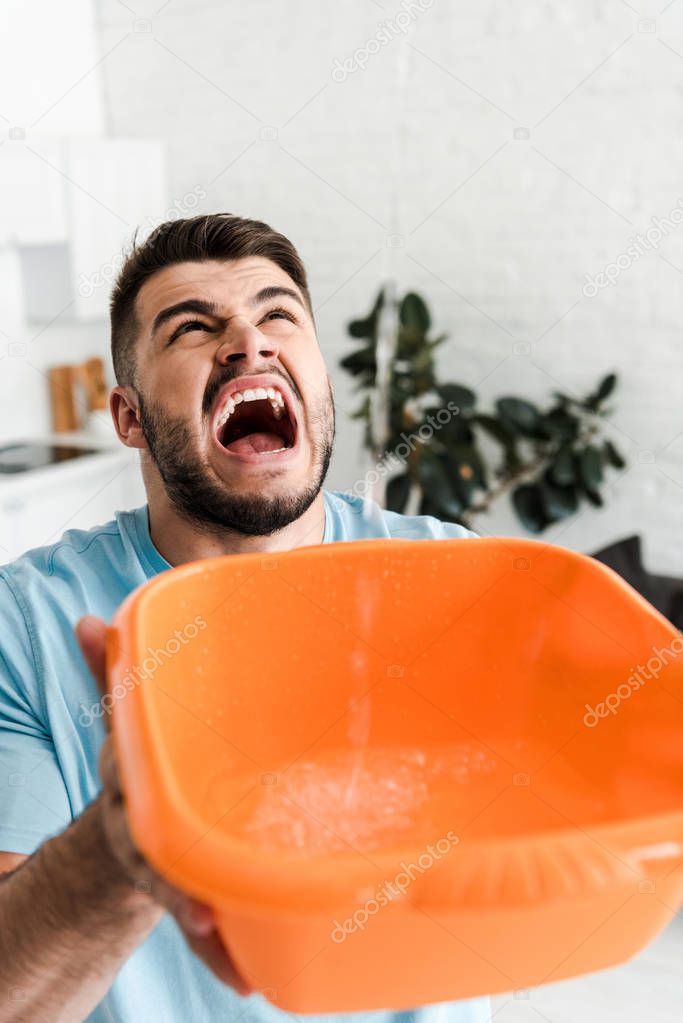 selective focus of screaming man holding plastic wash bowl near pouring water 
