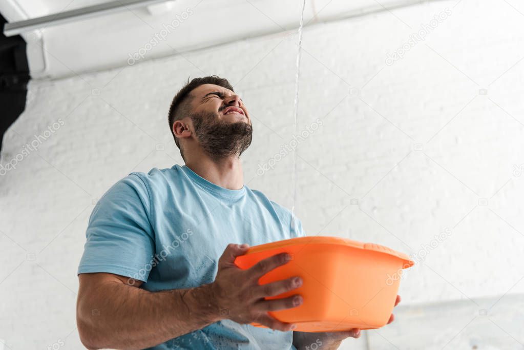 bearded man with closed eyes holding plastic wash bowl near pouring water 
