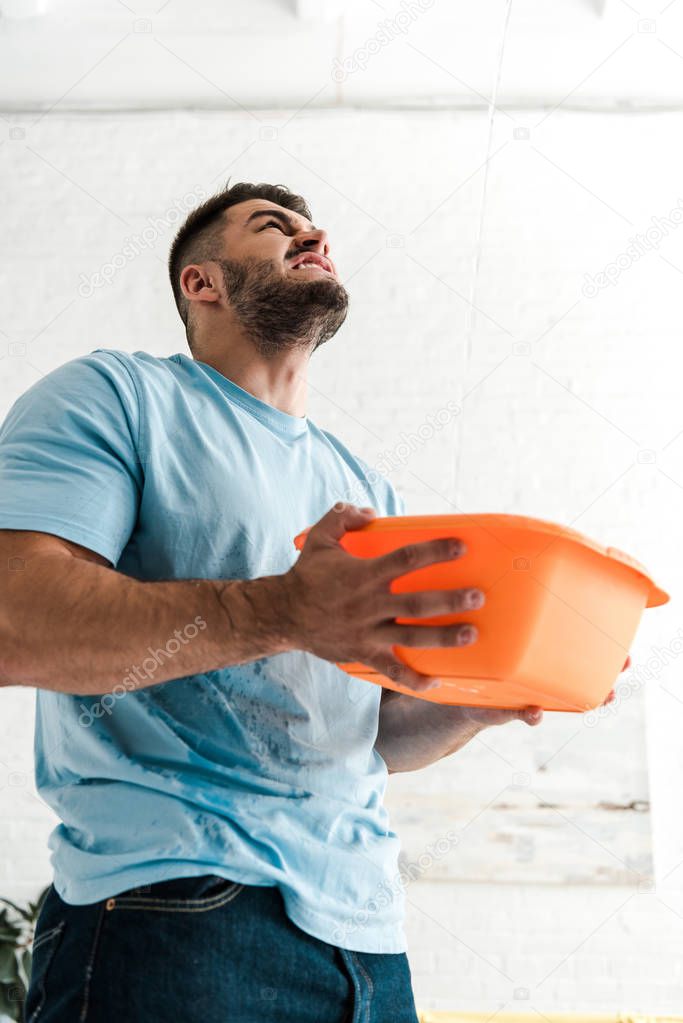 low angle view of bearded man holding plastic wash bowl near pouring water 