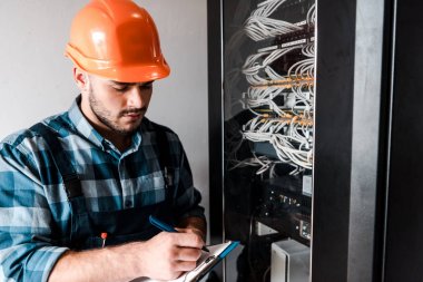 technician holding clipboard while writing near wires and cables  clipart