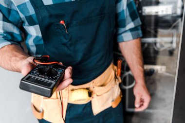 cropped view of technician holding digital meter near wires and cables  clipart