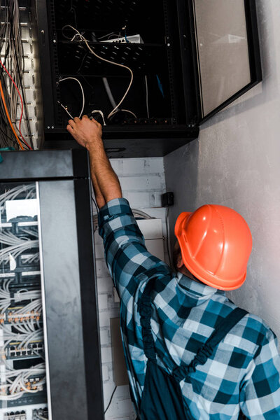 back view of man in safety helmet touching wires and cables 