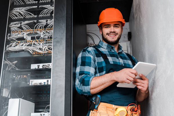 happy bearded technician in safety helmet holding digital tablet 