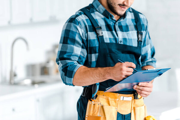 cropped view of of bearded workman holding clipboard and pen 