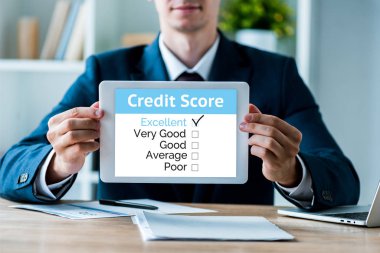 selective focus of happy man holding digital tablet with credit score letters in office  clipart
