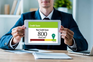 selective focus of happy man holding digital tablet with your credit score lettering in office  clipart