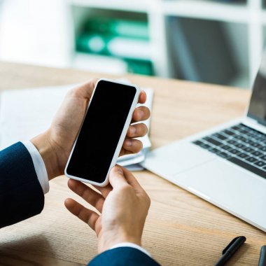 dizüstü bilgisayar ve kalem yanında boş ekran ile akıllı telefon tutan adam kırpılmış görünümü masada 