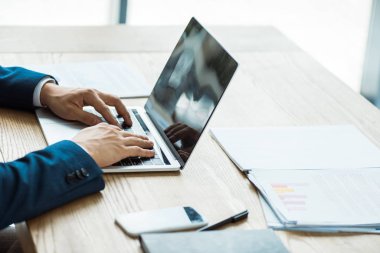 boş ekranlı akıllı telefonun yanındaki dizüstü bilgisayarda yazan işadamının kırpılmış görünümü