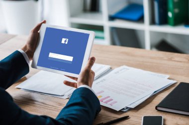 Kiev, Ukrayna - 8 Temmuz 2019: grafik ve grafiklere yakın ekranda facebook ile dijital tablet tutan adamın kırpılmış görünümü