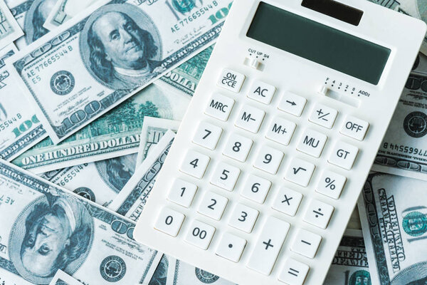 top view of white calculator on dollar banknotes 